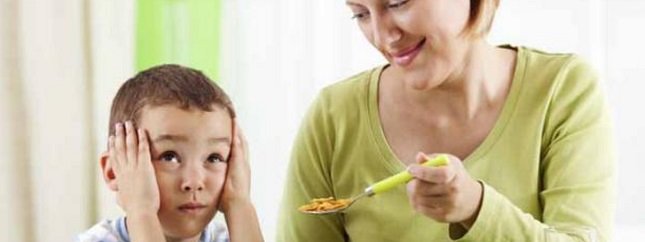 Fotografía de una mujer sosteniendo una cuchara de alimento frente a un niño